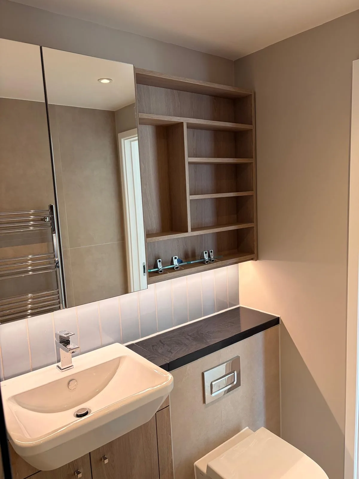En-suite with tiled walls, a fitted vanity unit, a mirrored recess with shelving and a heated towel rail.