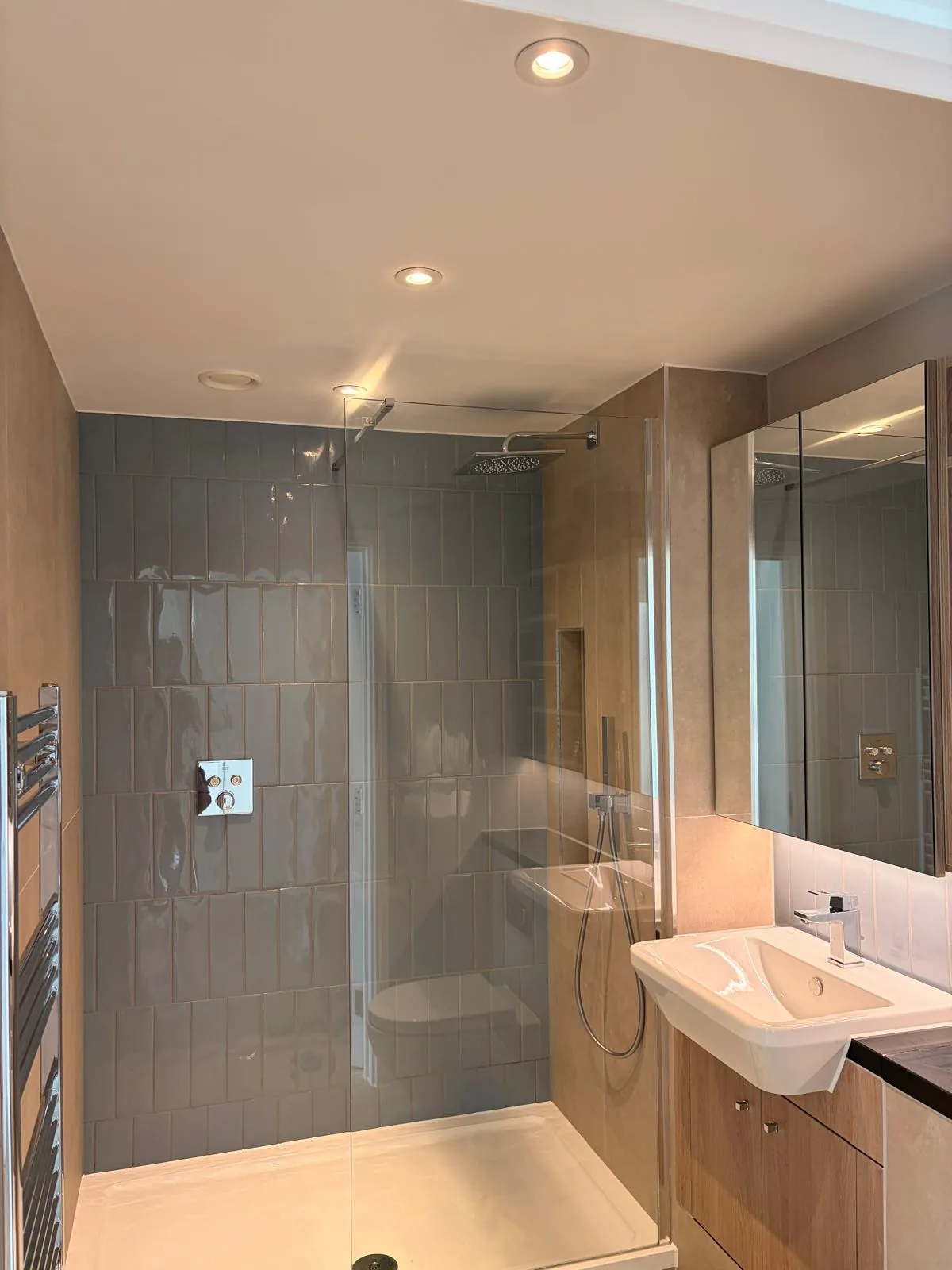 Shower room with grey wall tiling, a glazed shower screen, fitted vanity unit and heated towel rail.