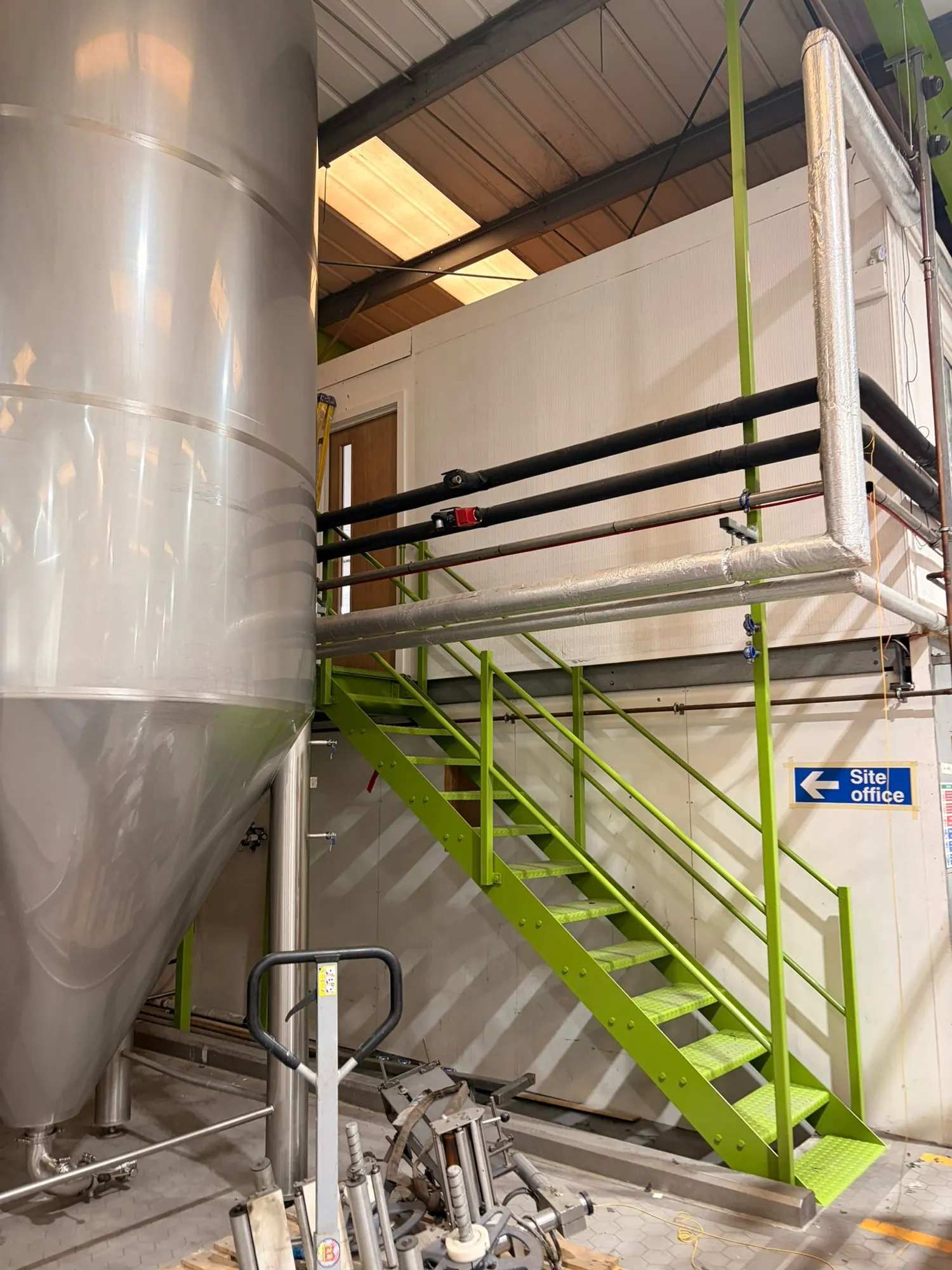 Green-coated steel access stair and handrail beside a large production vessel.