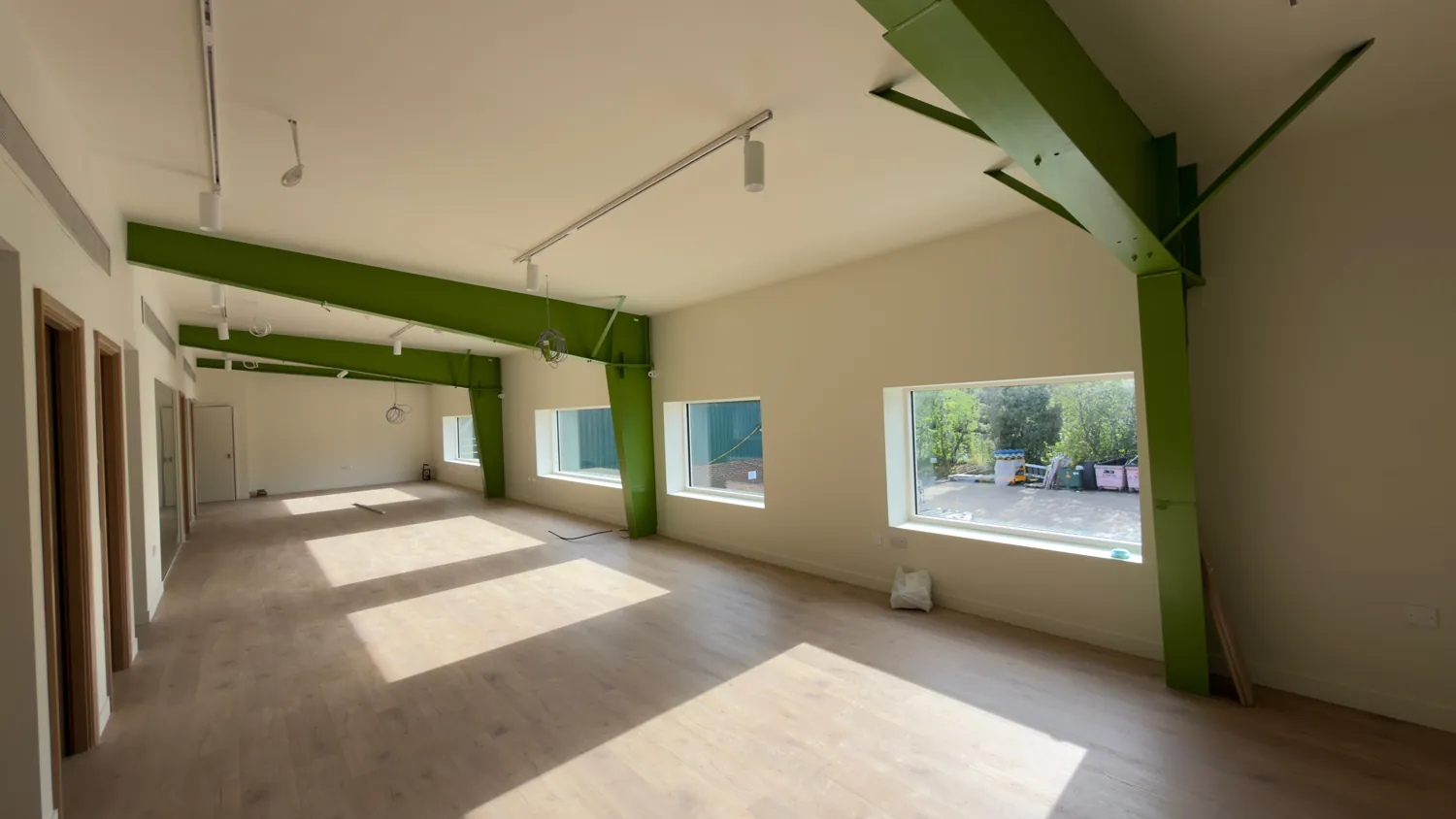 A run of green steel beams above a line of windows in an office space.