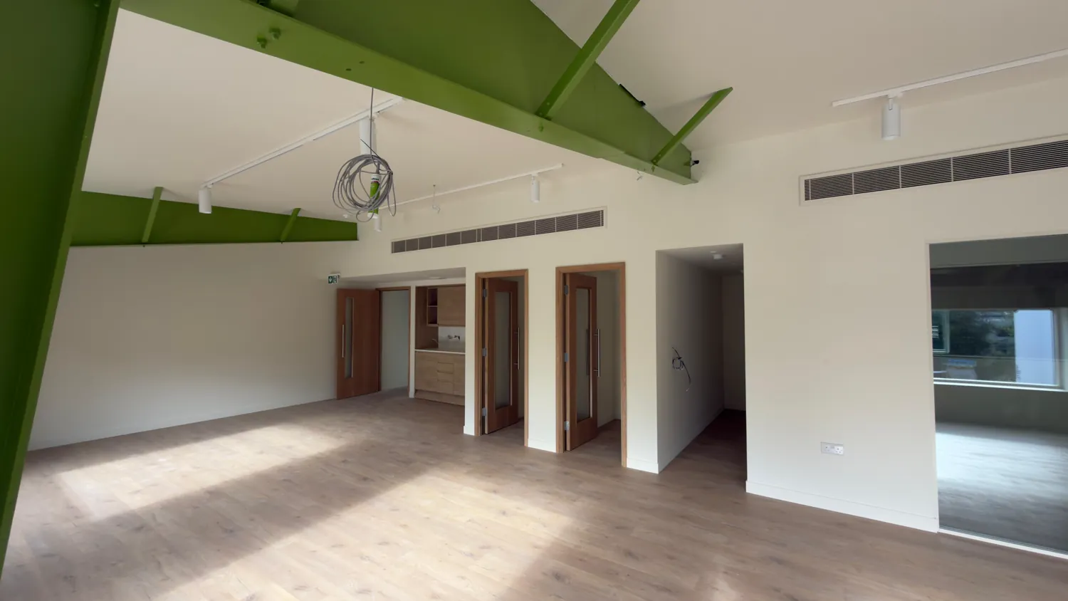 Green steel columns and beams with doorways through to side rooms.