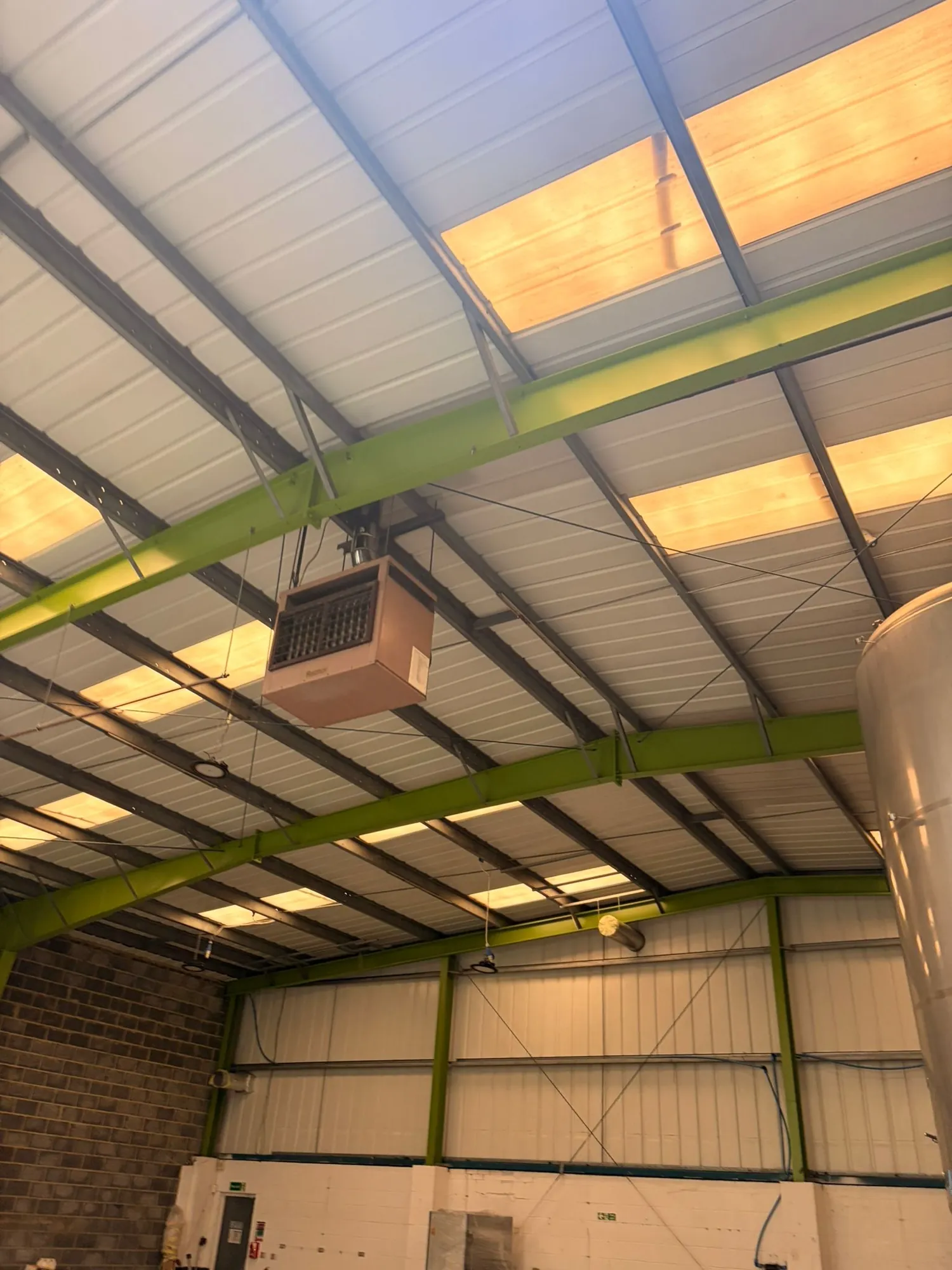 Warehouse roof structure of green steel beams beneath rooflights.