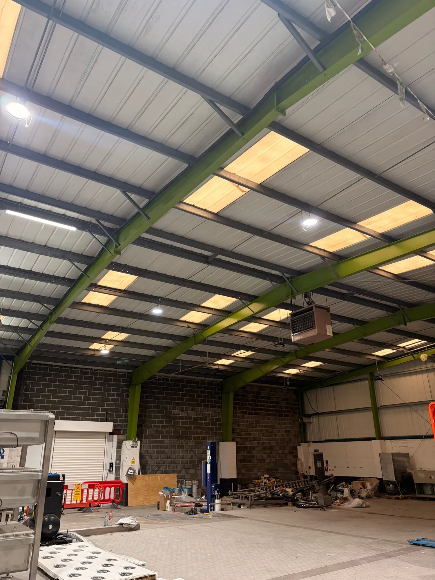 Warehouse interior showing a green steel frame, rooflights and a dark blockwork gable wall.