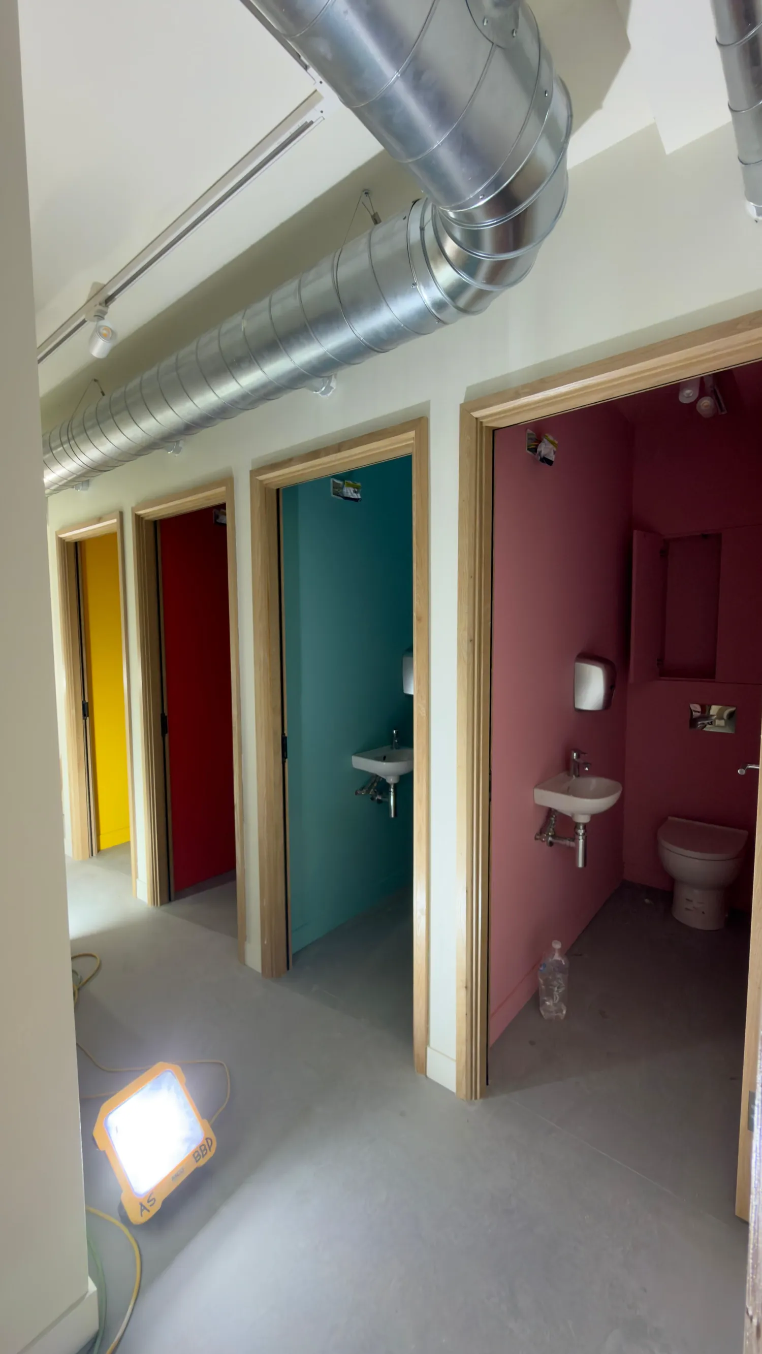 A run of WC compartments, each decorated in a different colour: yellow, red, teal and deep pink.