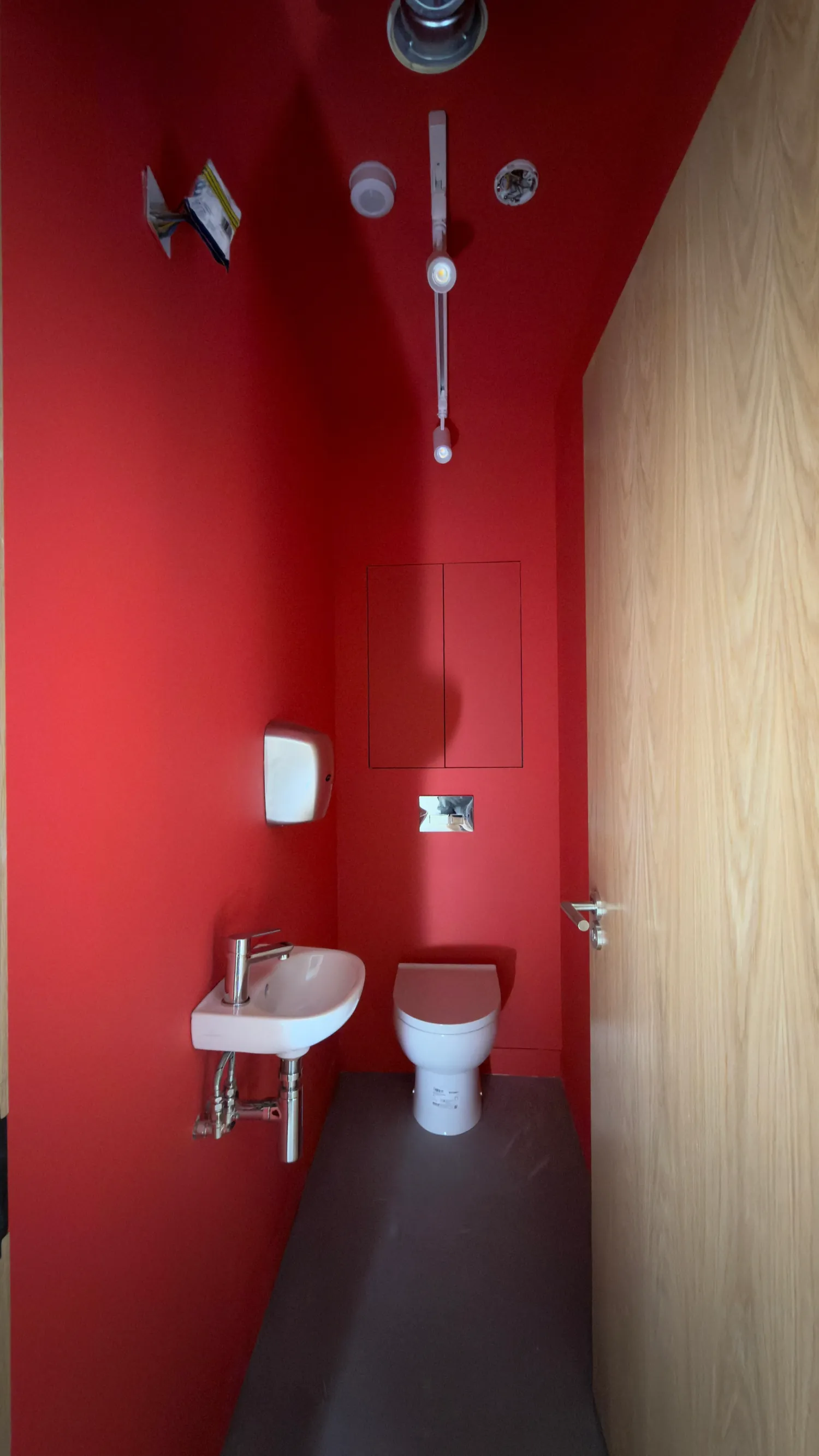 A WC compartment with walls and ceiling decorated red, a timber door and a dark floor.